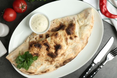 Photo of Delicious calzone served with sauce on grey table, flat lay