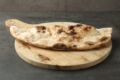 Photo of One delicious calzone on grey textured table, closeup