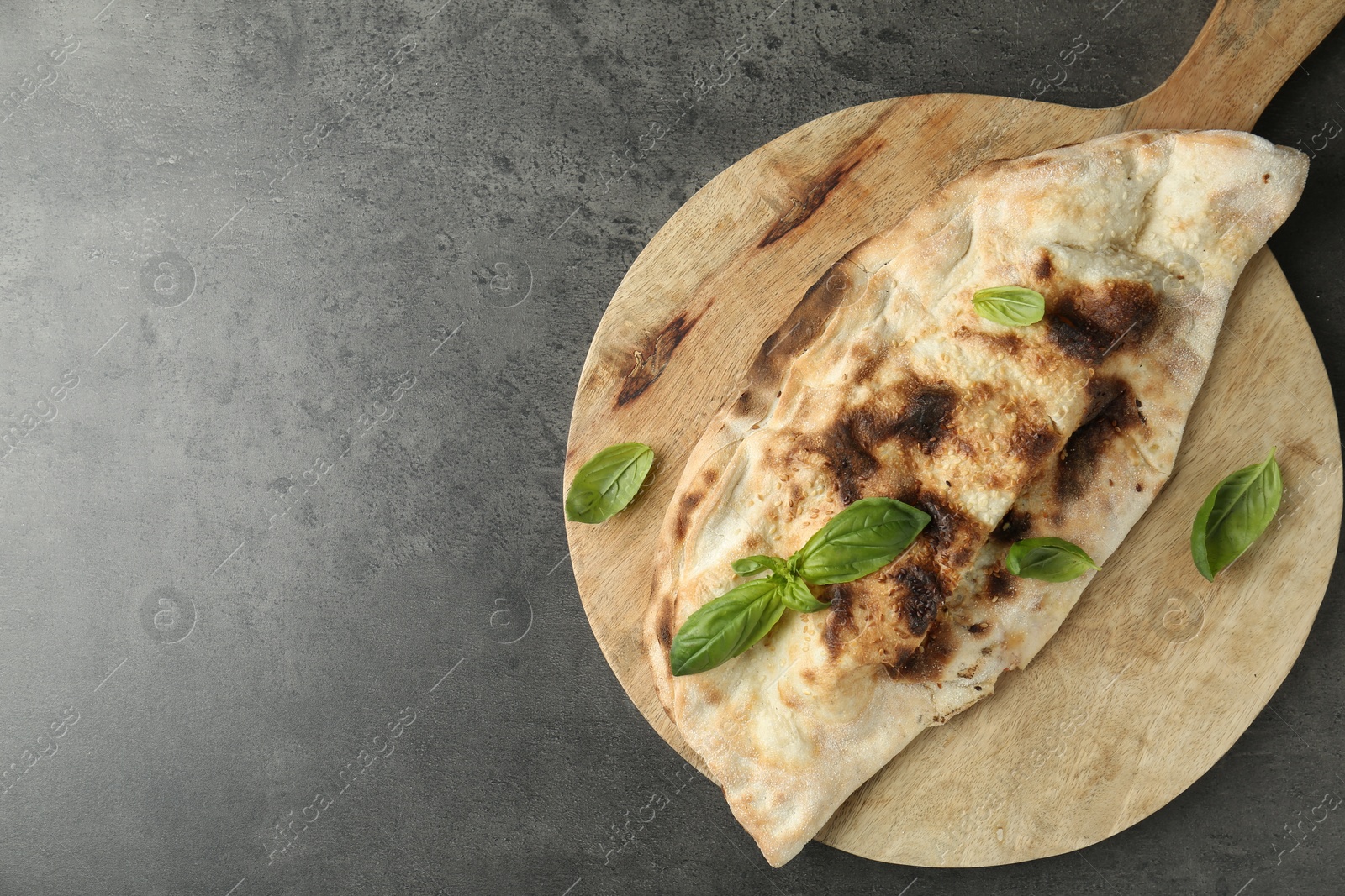 Photo of Delicious calzone with fresh basil on grey textured table, top view. Space for text