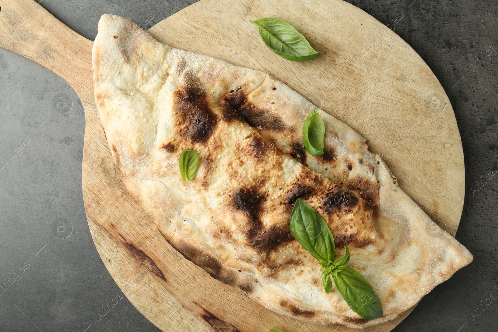 Photo of Delicious calzone with fresh basil on grey textured table, top view