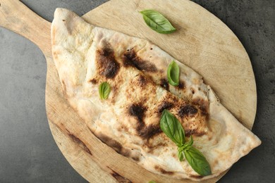 Delicious calzone with fresh basil on grey textured table, top view