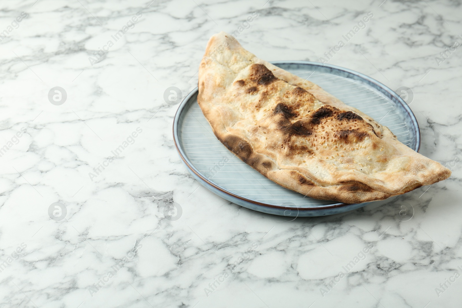 Photo of Delicious calzone on white marble table. Space for text