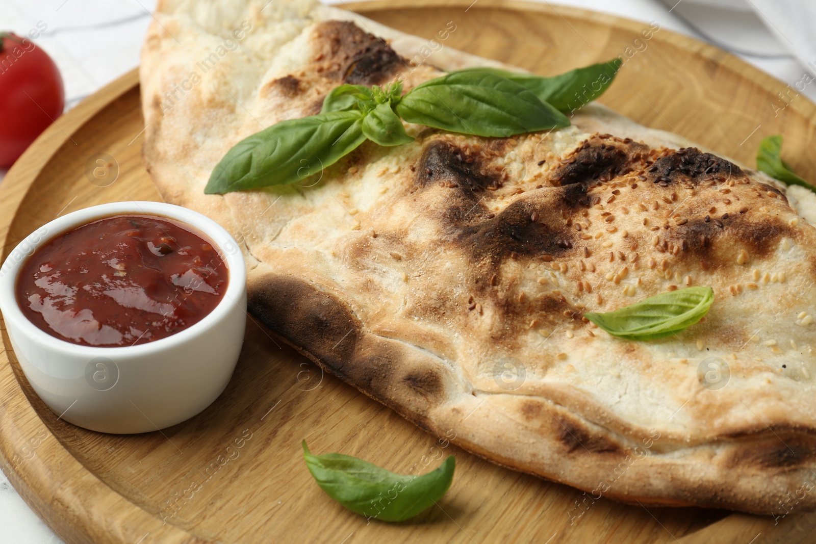 Photo of Delicious calzone with fresh basil and ketchup on table, closeup