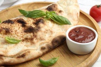 Photo of Delicious calzone with fresh basil and ketchup on table, closeup