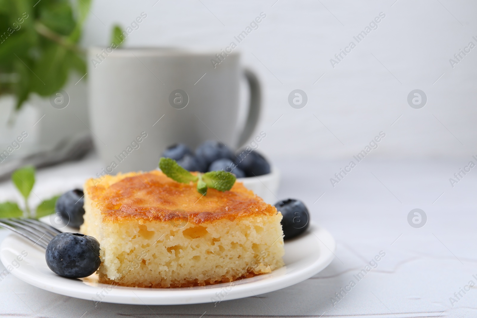 Photo of Slice of tasty semolina cake served on white textured table, closeup. Space for text