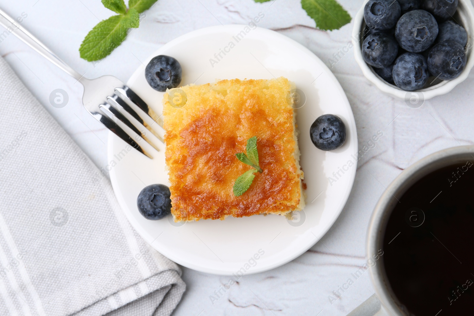 Photo of Slice of tasty semolina cake served on white textured table, flat lay