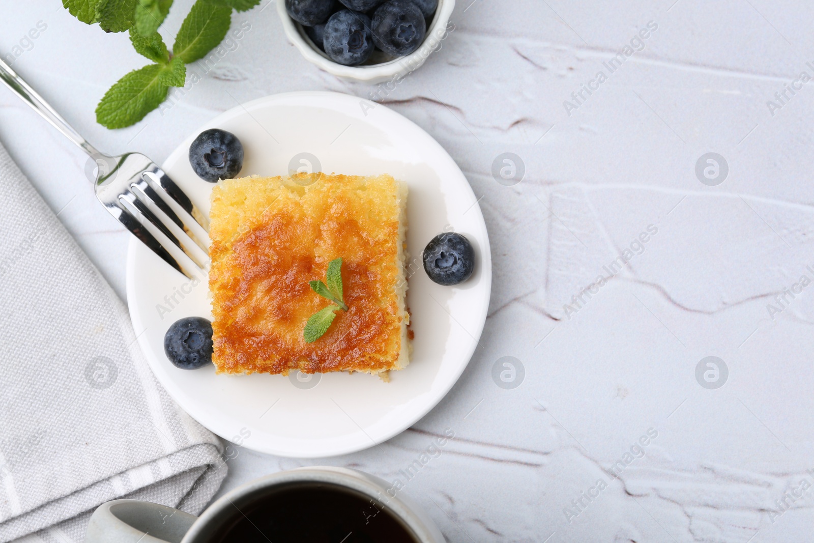 Photo of Slice of tasty semolina cake served on white textured table, flat lay. Space for text