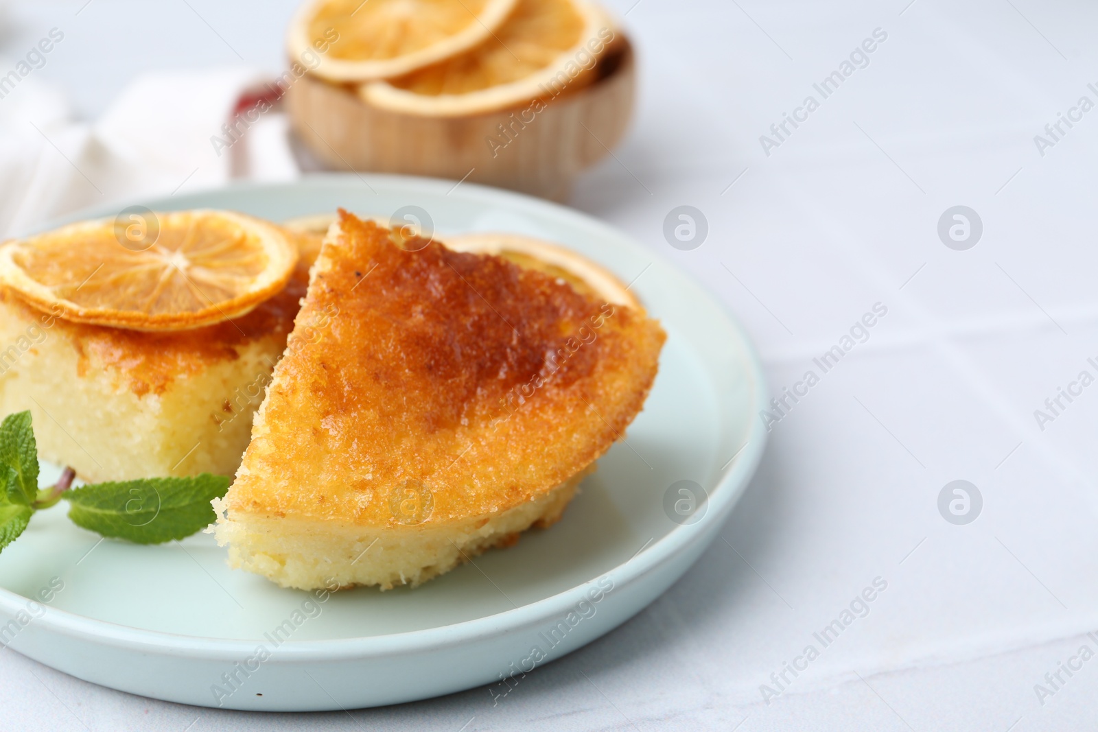 Photo of Tasty semolina cake served on white tiled table, closeup. Space for text