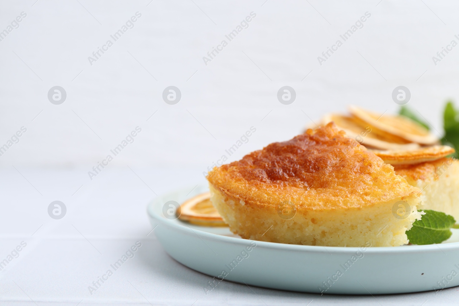 Photo of Tasty semolina cake served on white tiled table, closeup. Space for text