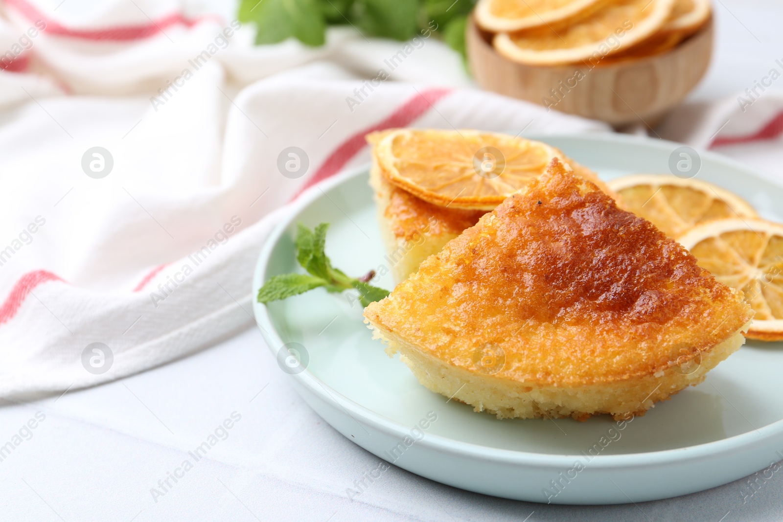 Photo of Slice of tasty semolina cake served on white tiled table, closeup. Space for text