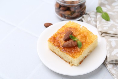 Photo of Slice of tasty semolina cake served on white tiled table, closeup. Space for text