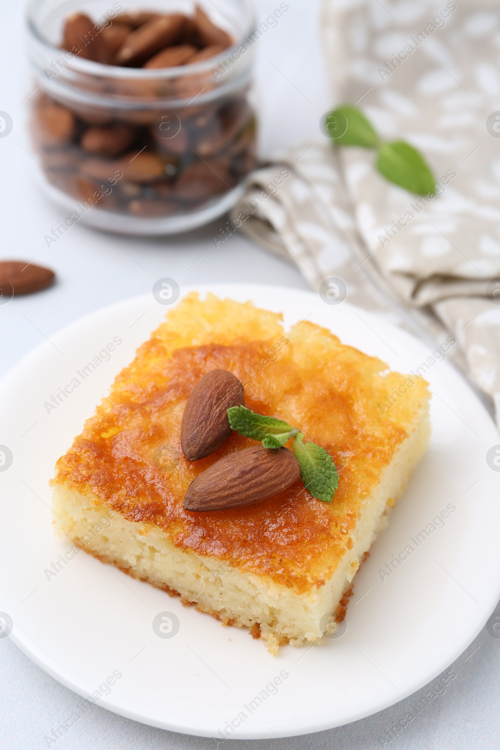 Photo of Slice of tasty semolina cake served on white tiled table, closeup