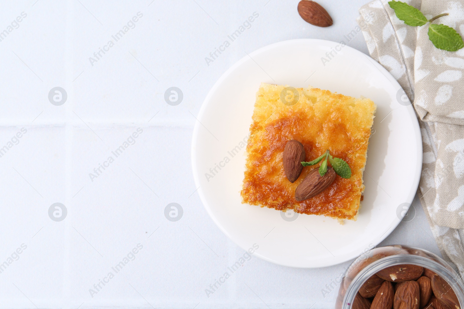 Photo of Slice of tasty semolina cake served on white tiled table, flat lay. Space for text