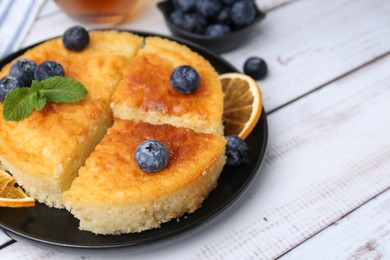 Photo of Delicious semolina cake with blueberries and orange slices on white wooden table, closeup. Space for text