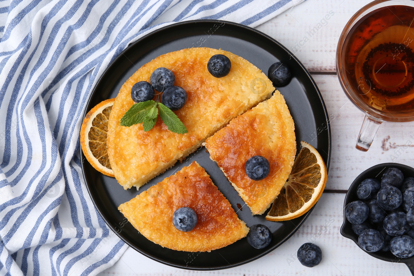 Photo of Delicious semolina cake with blueberries and orange slices on white wooden table, flat lay