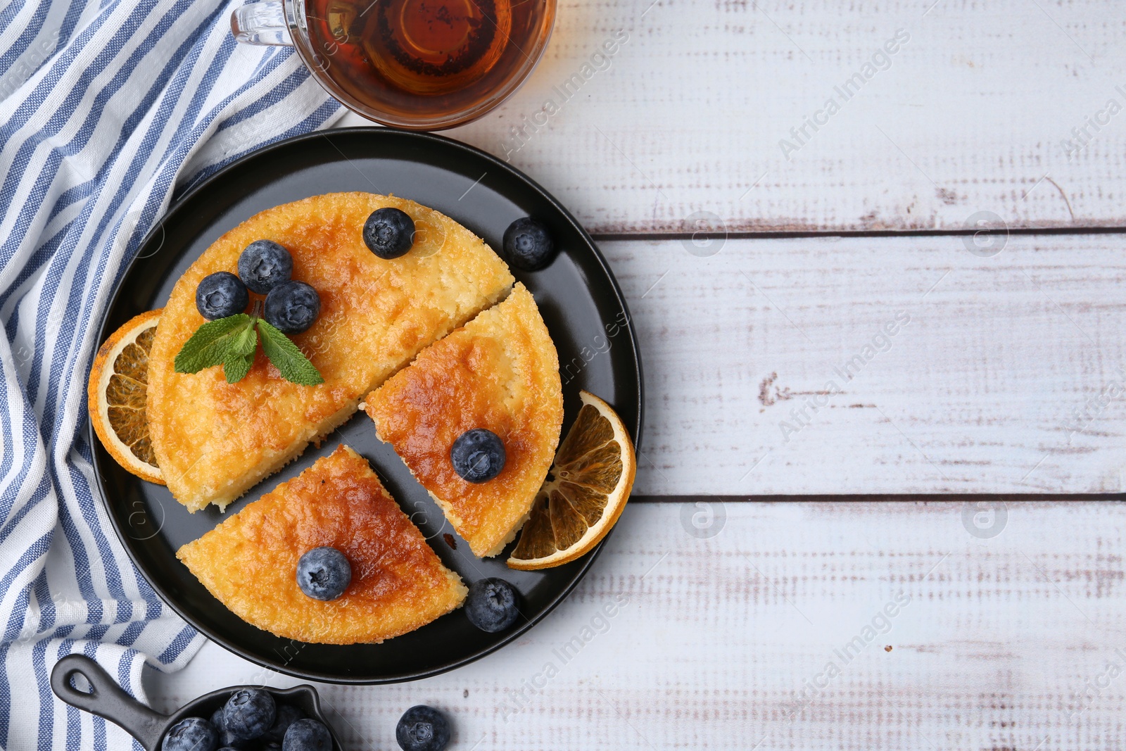 Photo of Delicious semolina cake with blueberries and orange slices on white wooden table, flat lay. Space for text