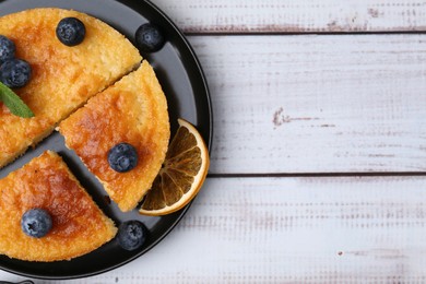 Photo of Delicious semolina cake with blueberries and orange slices on white wooden table, top view. Space for text