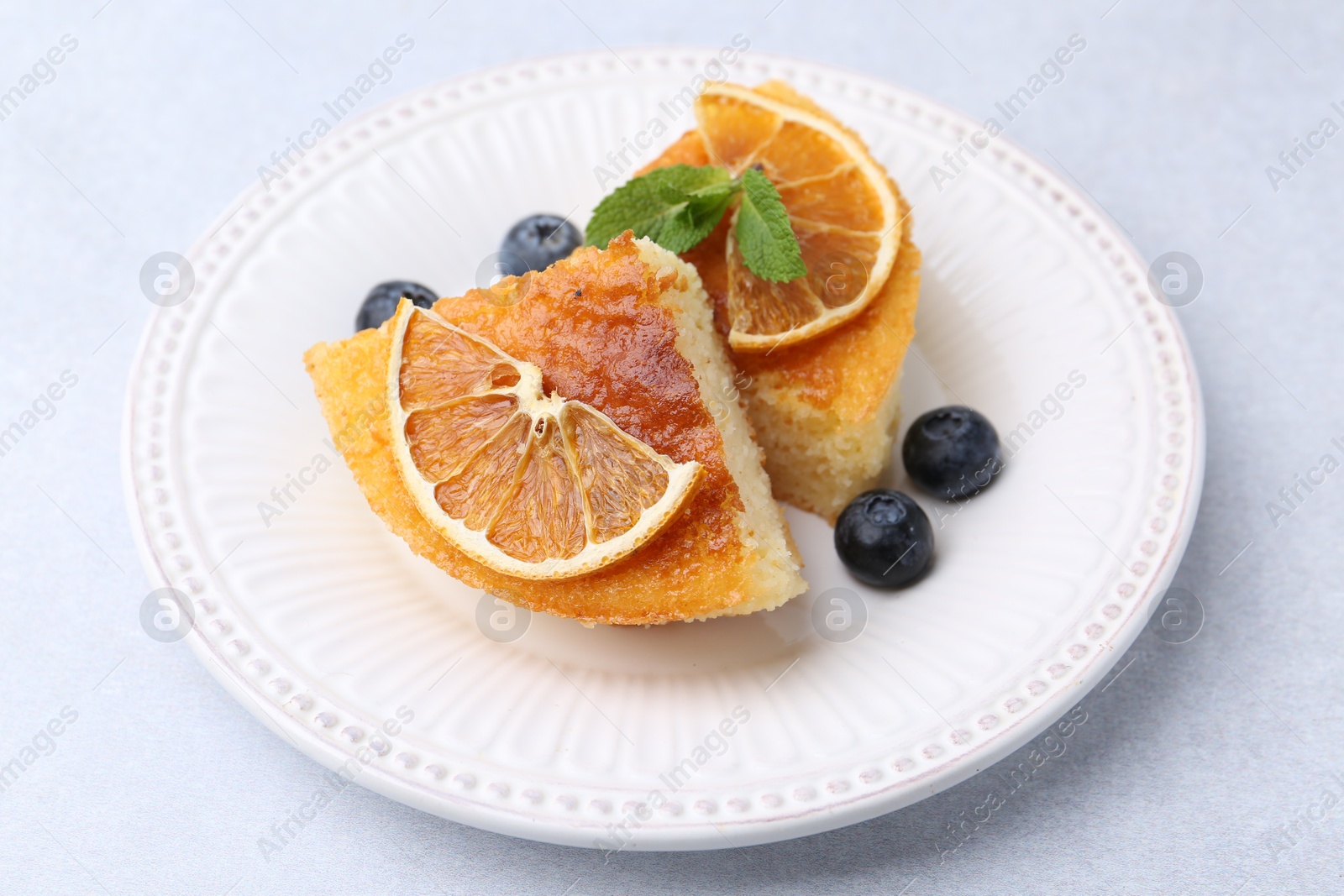 Photo of Pieces of delicious semolina cake with blueberries and orange slices on light table, closeup