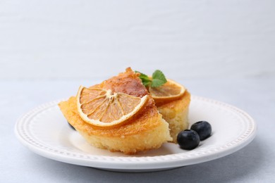 Pieces of delicious semolina cake with blueberries and orange slices on light table, closeup