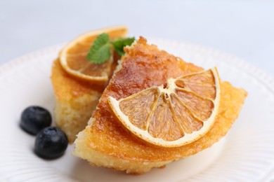 Photo of Pieces of delicious semolina cake with blueberries and orange slices on light table, closeup