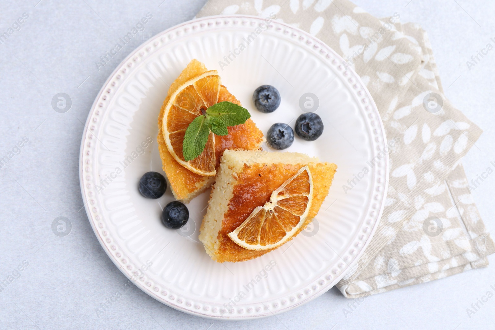 Photo of Pieces of delicious semolina cake with blueberries and orange slices on light table, top view