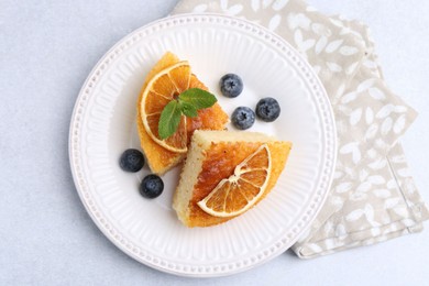 Photo of Pieces of delicious semolina cake with blueberries and orange slices on light table, top view