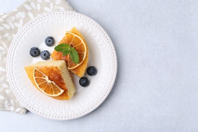 Photo of Pieces of delicious semolina cake with blueberries and orange slices on light table, top view. Space for text