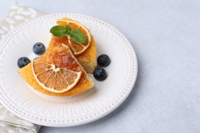 Photo of Pieces of delicious semolina cake with blueberries and orange slices on light table