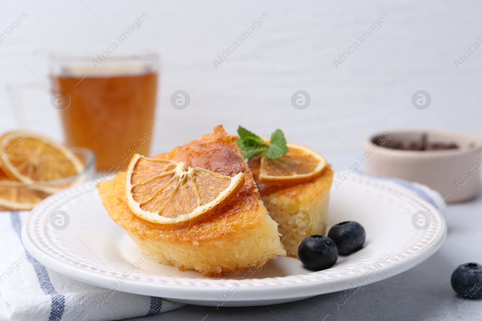 Photo of Pieces of delicious semolina cake with blueberries and orange slices on light table, closeup