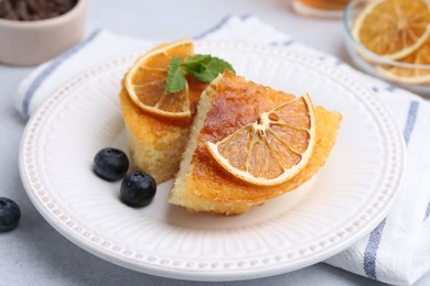 Photo of Pieces of delicious semolina cake with blueberries and orange slices on light table, closeup