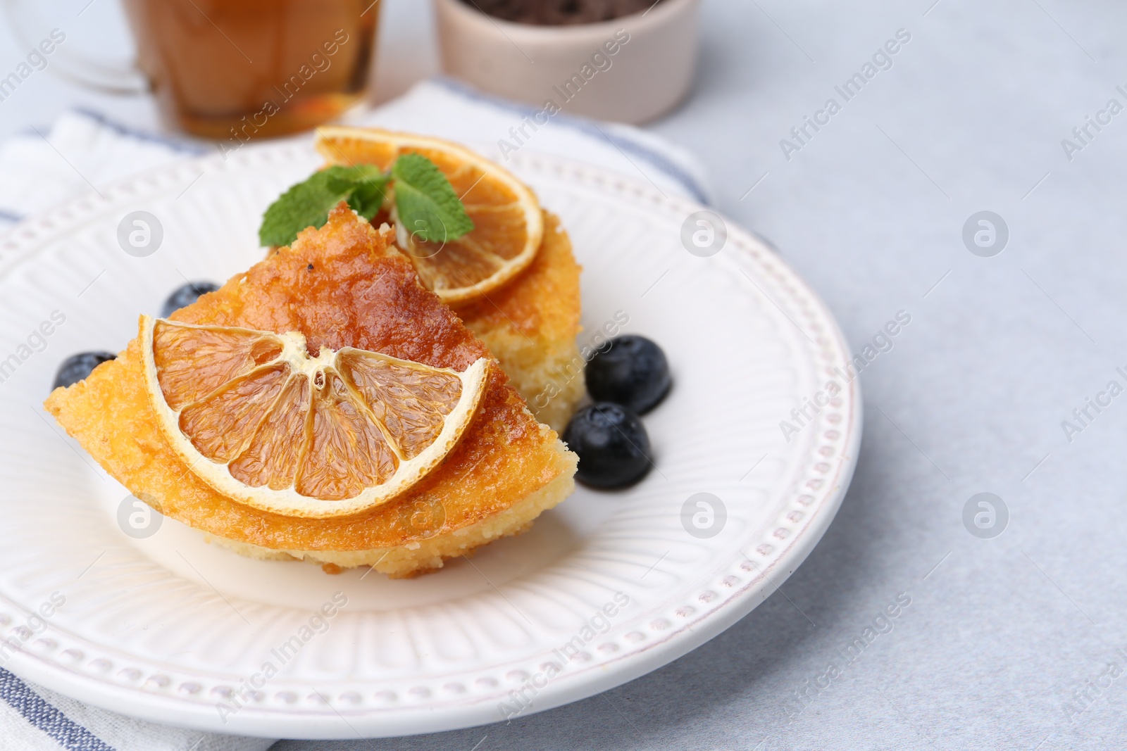 Photo of Pieces of delicious semolina cake with blueberries and orange slices on light table, closeup