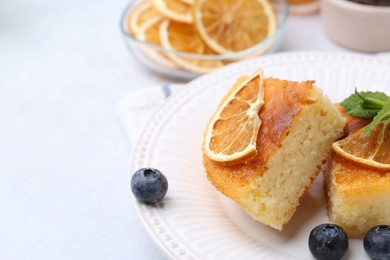 Photo of Pieces of delicious semolina cake with blueberries and orange slices on light table, closeup. Space for text