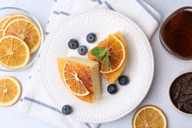 Photo of Pieces of delicious semolina cake with blueberries and orange slices on light table, flat lay