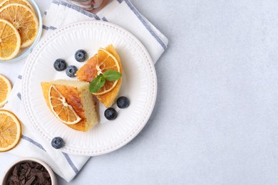 Photo of Pieces of delicious semolina cake with blueberries and orange slices on light table, flat lay. Space for text