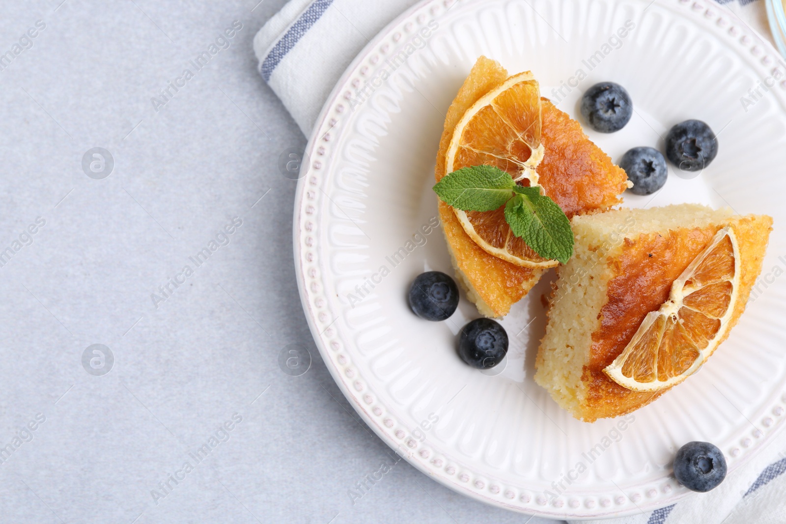 Photo of Pieces of delicious semolina cake with blueberries and orange slices on light table, top view. Space for text