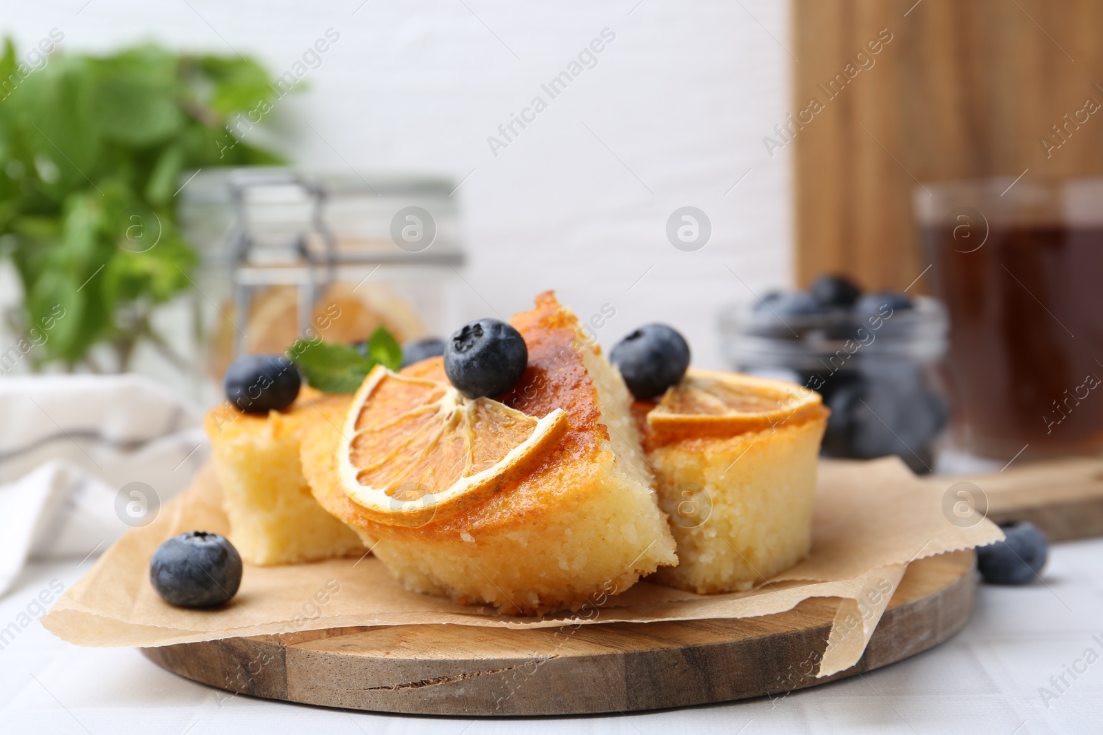 Photo of Pieces of delicious semolina cake with blueberries and orange slices on white tiled table, closeup