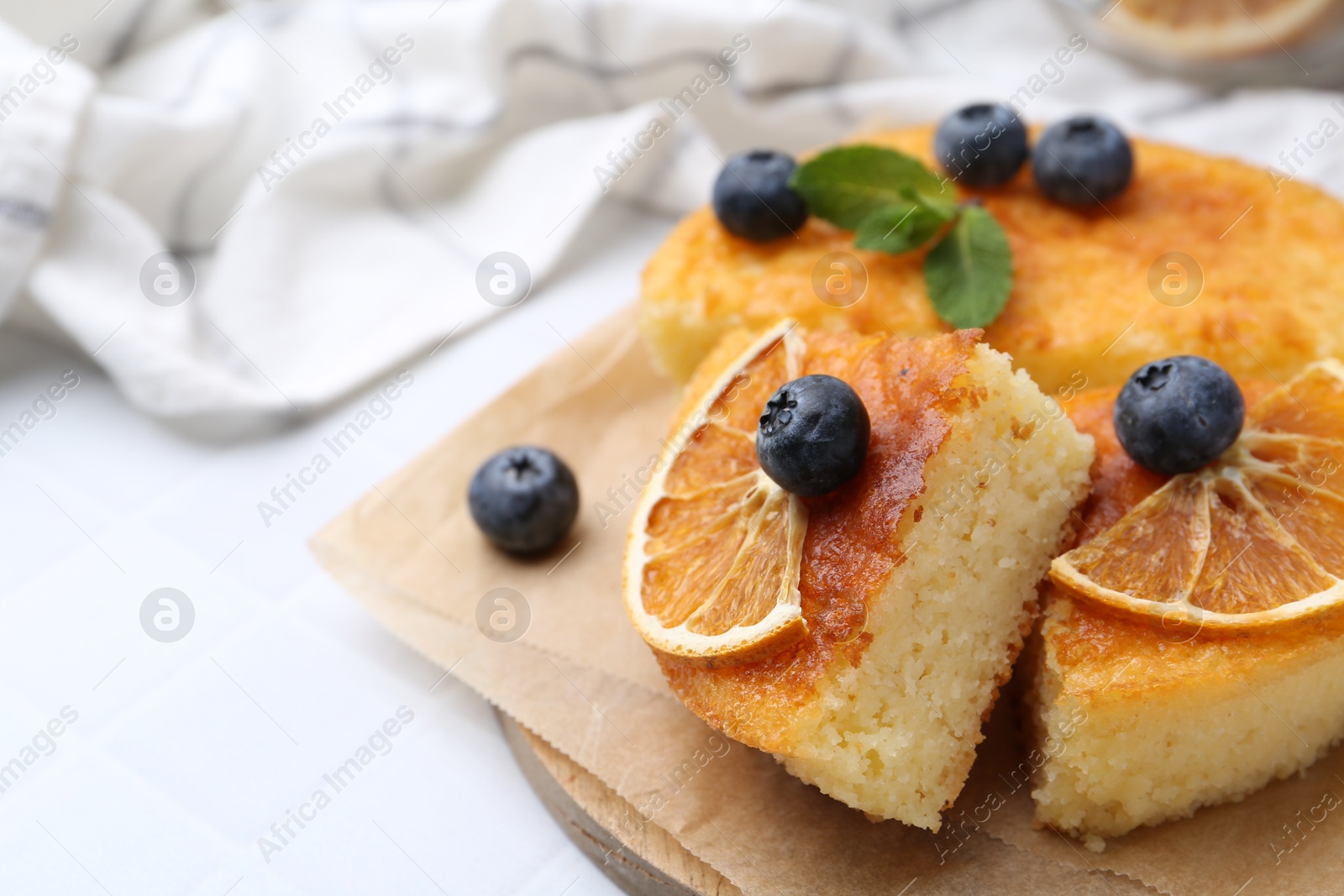 Photo of Pieces of delicious semolina cake with blueberries and orange slices on white tiled table, closeup. Space for text