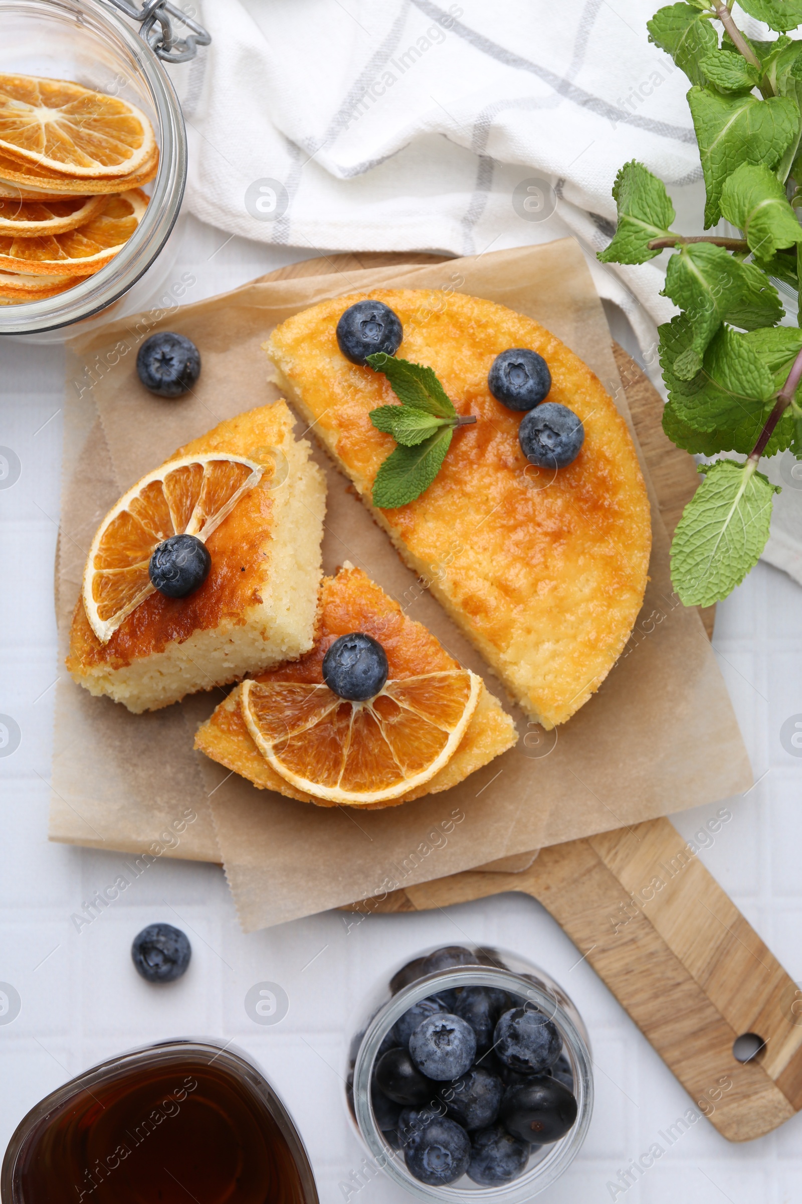 Photo of Pieces of delicious semolina cake with blueberries and orange slices on white tiled table, flat lay