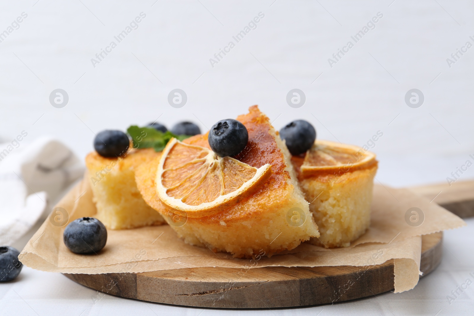 Photo of Pieces of delicious semolina cake with blueberries and orange slices on white tiled table, closeup