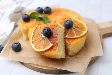 Photo of Pieces of delicious semolina cake with blueberries and orange slices on white tiled table, closeup