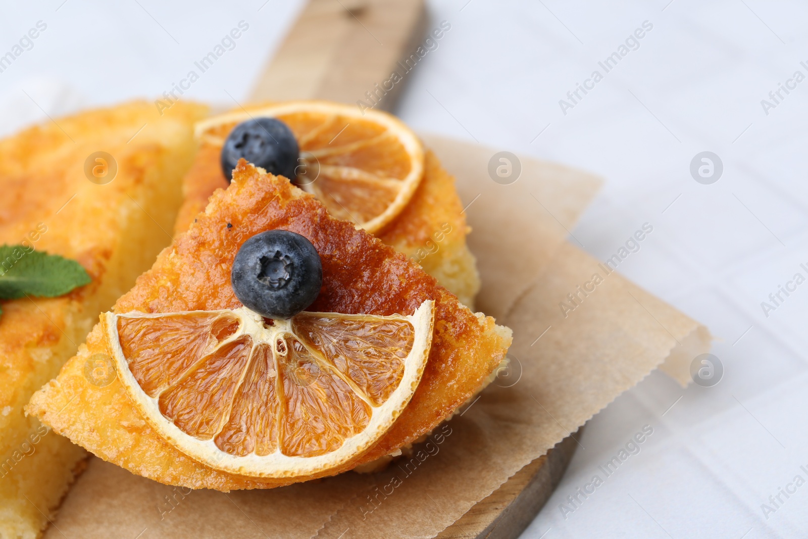 Photo of Pieces of delicious semolina cake with blueberries and orange slices on white tiled table, closeup