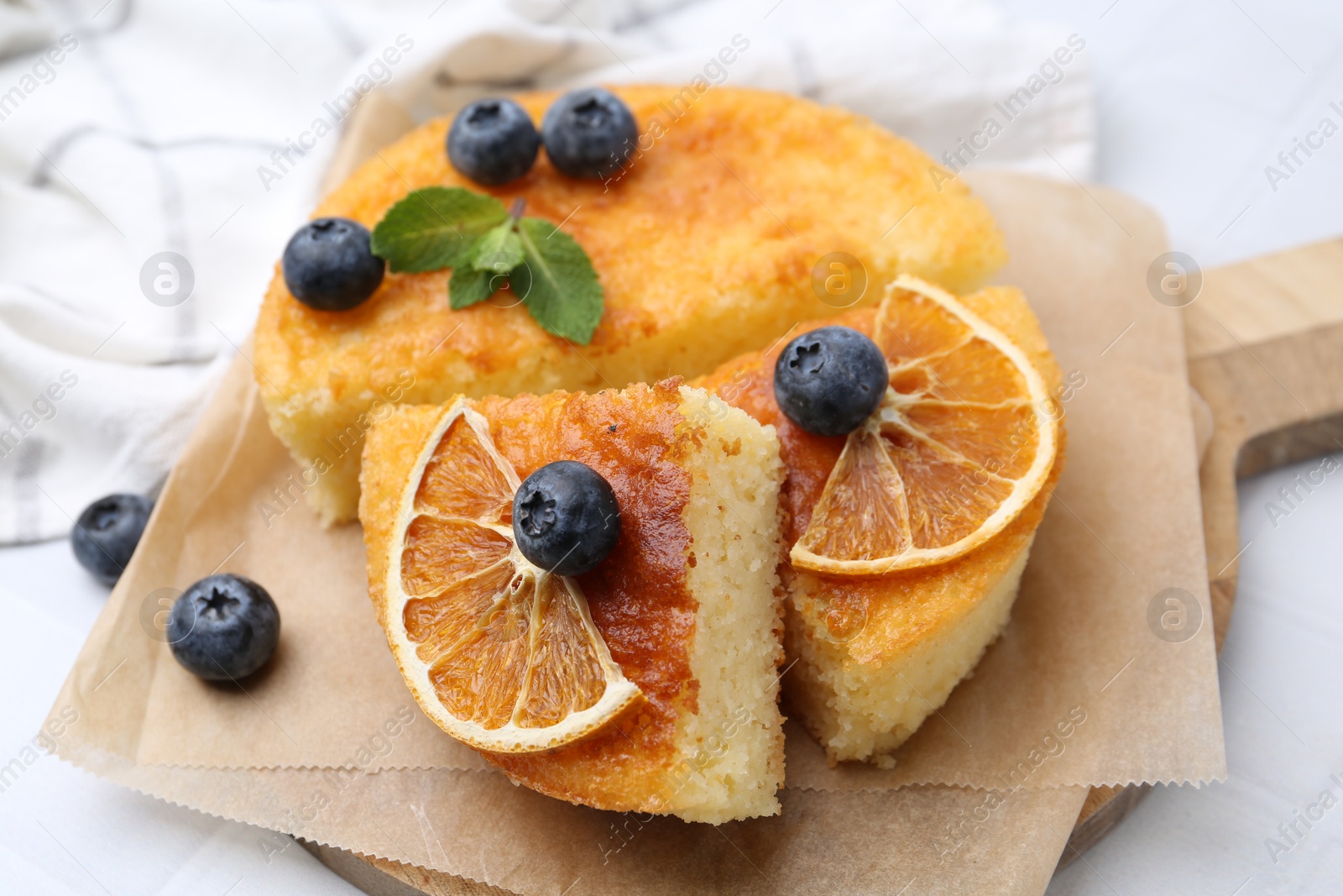 Photo of Pieces of delicious semolina cake with blueberries and orange slices on white tiled table, closeup