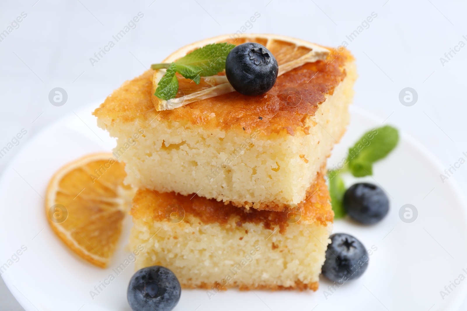 Photo of Pieces of delicious semolina cake with blueberries and orange slices on table, closeup