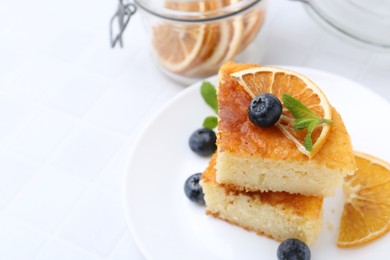 Photo of Pieces of delicious semolina cake with blueberries and orange slices on white table, closeup. Space for text