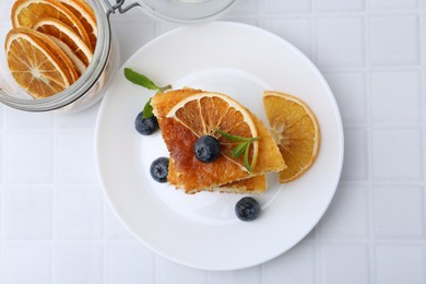 Pieces of delicious semolina cake with blueberries and orange slices on white tiled table, top view