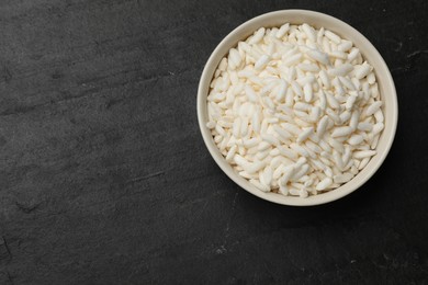 Photo of Puffed rice in bowl on dark table, top view. Space for text