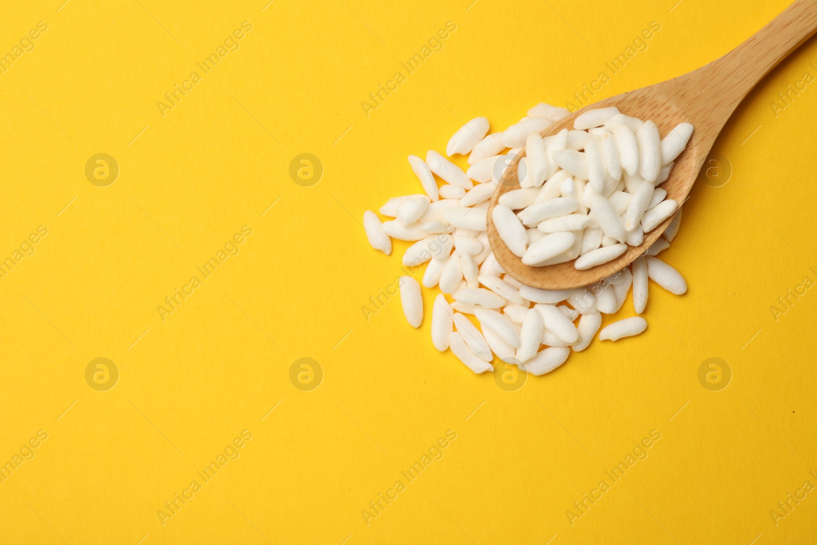 Photo of Spoon with puffed rice on yellow background, top view. Space for text