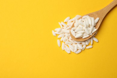 Photo of Spoon with puffed rice on yellow background, top view. Space for text