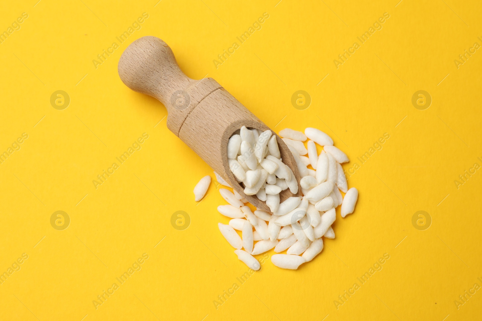 Photo of Scoop with puffed rice on yellow background, top view