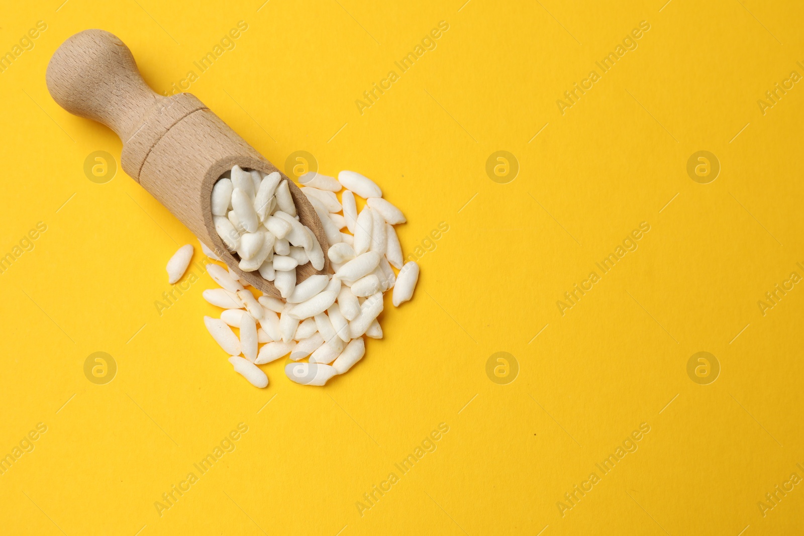 Photo of Scoop with puffed rice on yellow background, top view. Space for text